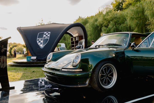 Green RCR restomod Porsche 911 displayed on a reflective platform at an outdoor event.