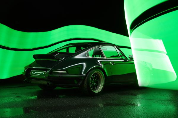 A sleek black sports car is parked on a wet surface at night, surrounded by dynamic green light trails creating a futuristic effect. The cars license plate reads RCR.